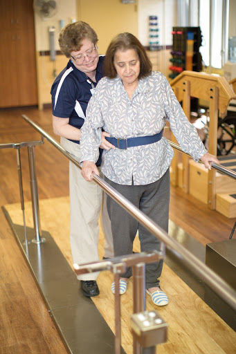 A physical therapist assists an elderly patient during rehabilitation, helping them navigate a ramp.