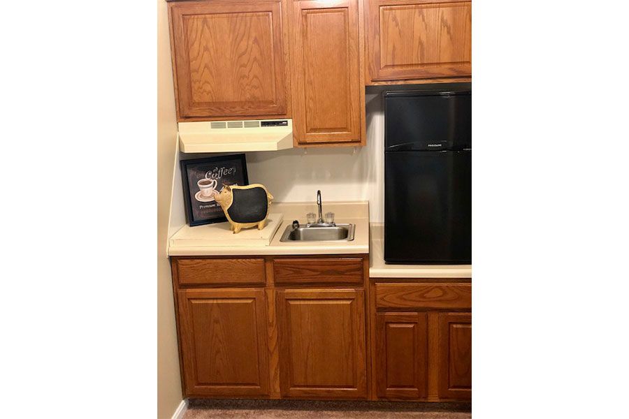 A compact kitchen setup with wooden cabinets, a microwave, a small sink, and a refrigerator.