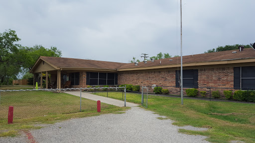 An exterior view of a brick building, possibly a school, surrounded by grass and pathways.