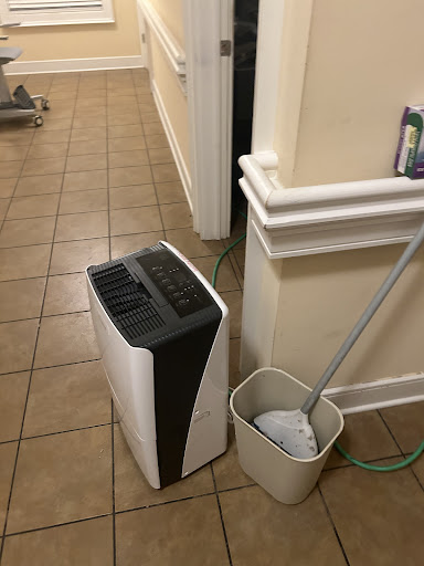 A dehumidifier placed next to a mop and bucket in a tiled hallway.