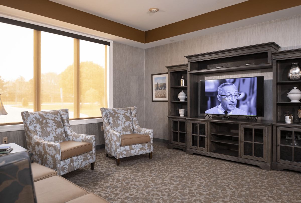 A cozy living room with patterned chairs and a television playing a black-and-white film.
