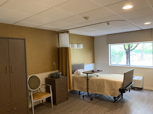 A view of a hospital patient room featuring a bed, chair, and window.