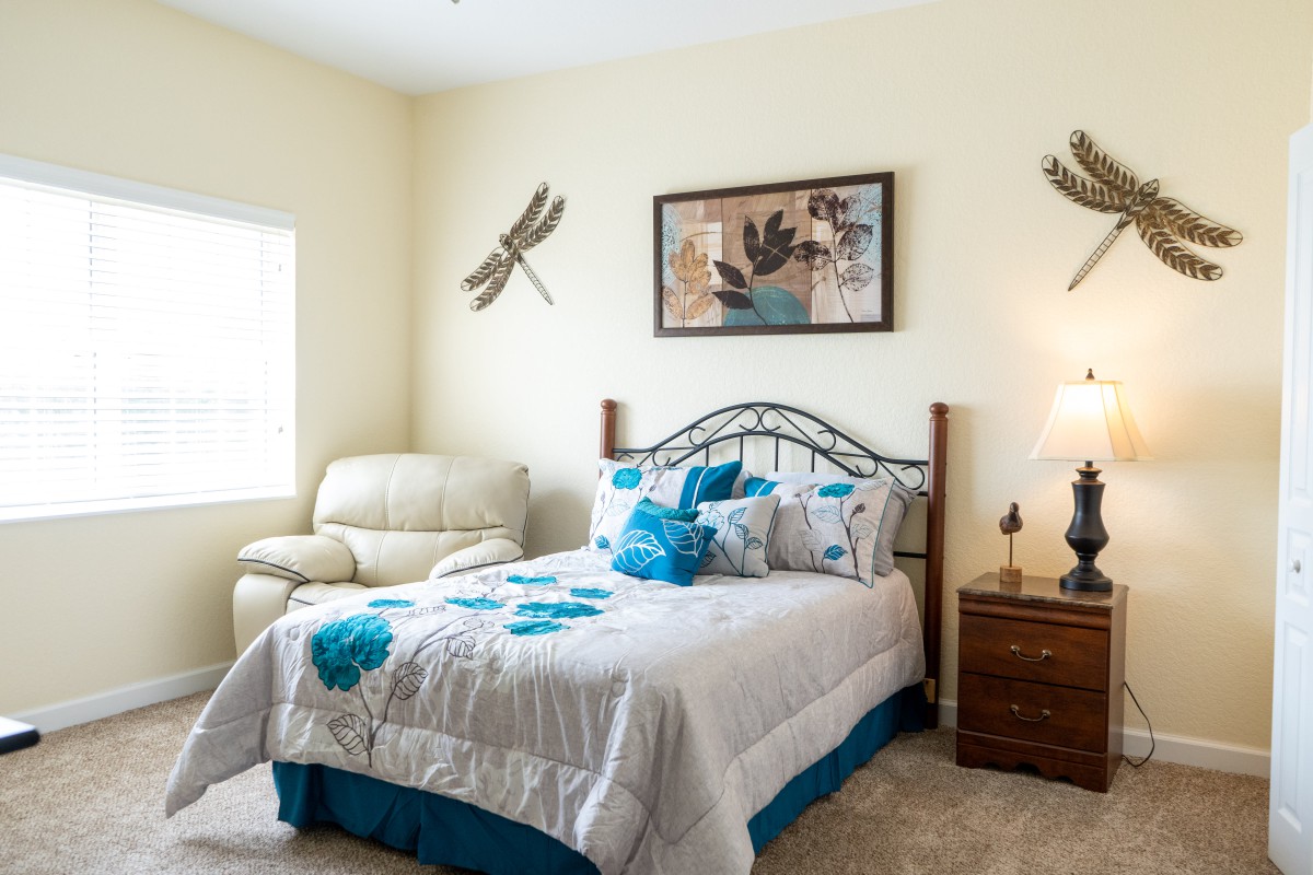 A cozy bedroom with dragonfly-themed decor, featuring a comfortable armchair and a well-made bed.
