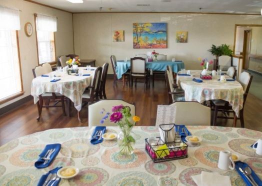 A neatly arranged dining room with several tables set for a meal, adorned with flowers and colorful decor.
