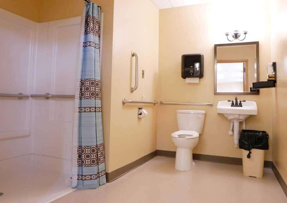 An accessible bathroom featuring a toilet, sink, and shower with grab bars for added safety.