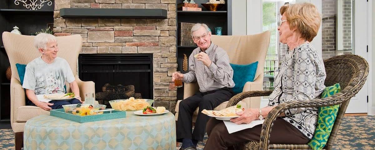 An elderly man enjoying snacks and a drink in a cozy living room by the fireplace.