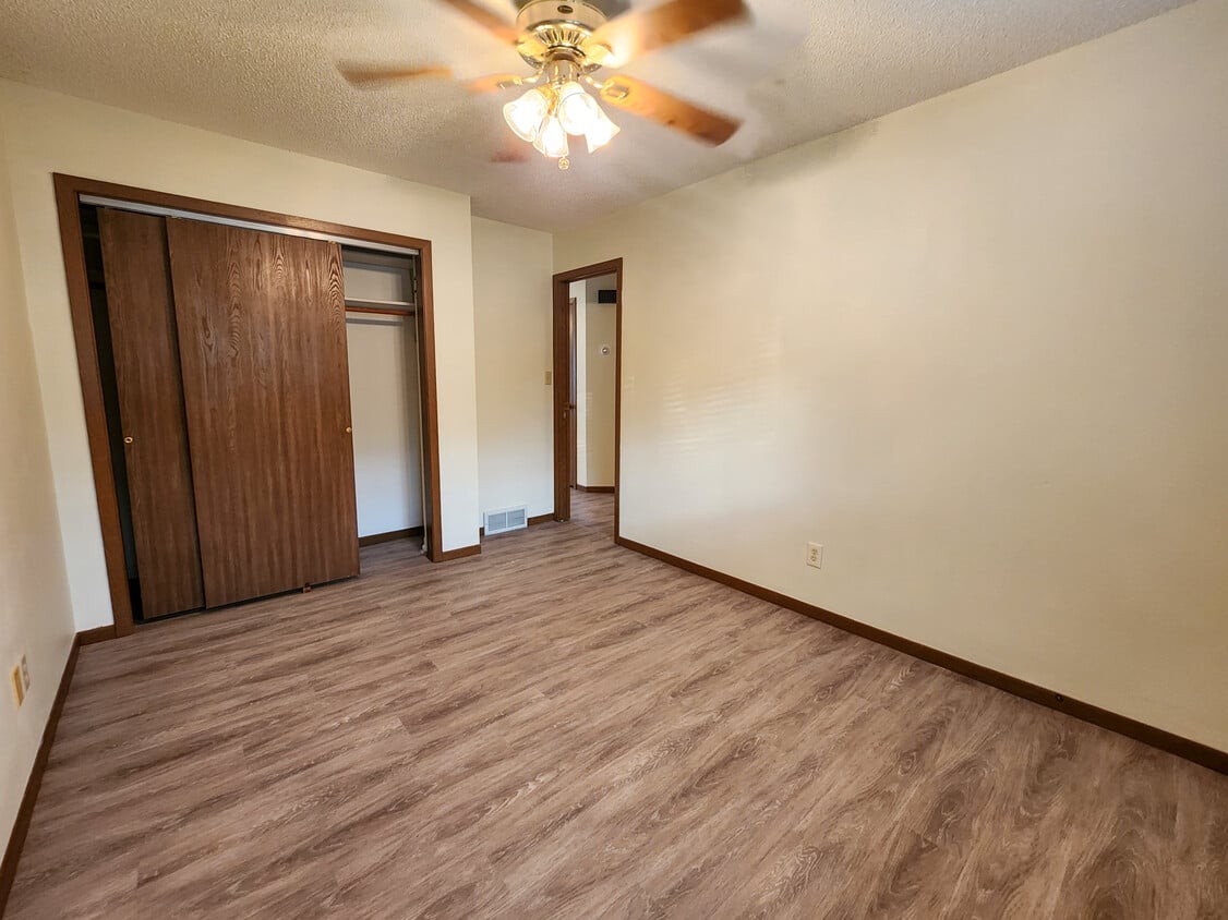 An empty room featuring a wooden floor, ceiling fan, and built-in closet.