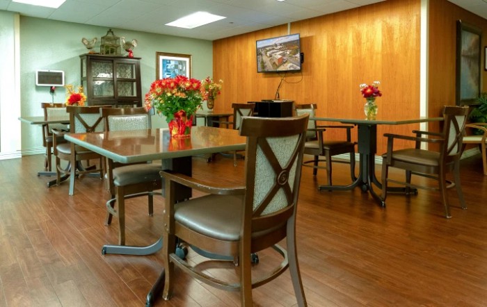 A dining area with tables and chairs, decorated with vases of flowers and a television mounted on the wall.