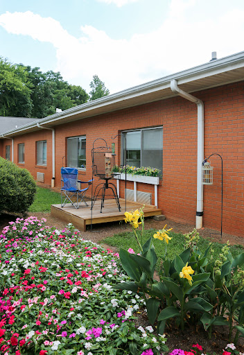 A cozy outdoor patio area with vibrant flowers and a brick house backdrop.