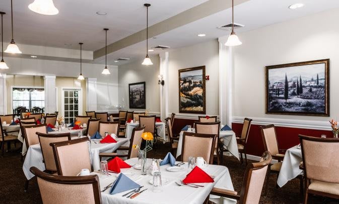 A well-lit dining area with neatly arranged tables, adorned with colorful napkins and elegant chairs, surrounded by framed artwork.