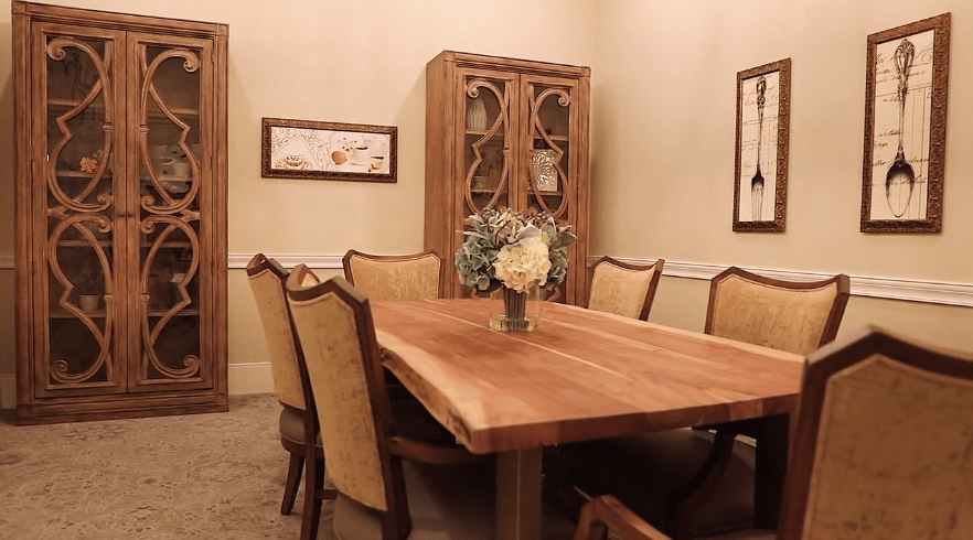 A cozy dining room with a wooden table and upholstered chairs, featuring a decorative cabinet in the background.