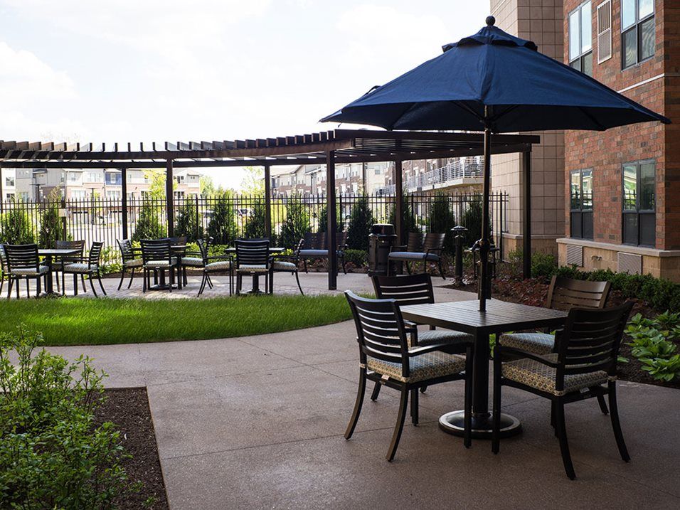 A peaceful outdoor patio area with tables, chairs, and umbrellas set against a backdrop of lush greenery.