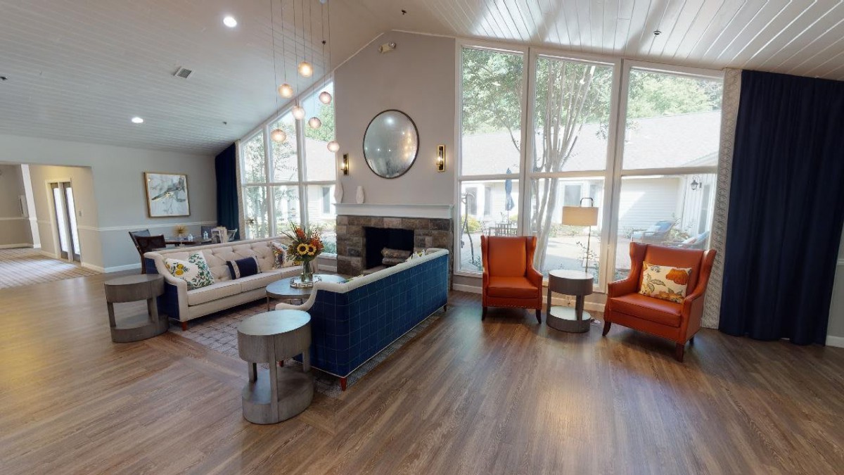A modern living room with a cozy seating area, featuring a sofa and orange armchairs, complemented by large windows and a fireplace.