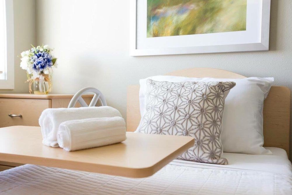 A neatly arranged bedroom with a decorative pillow and rolled towels on a tray table.