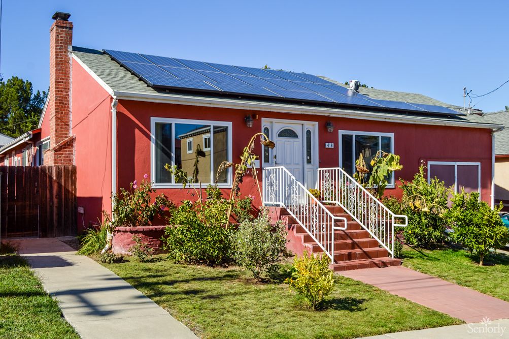 A charming red house with solar panels and a well-maintained garden.