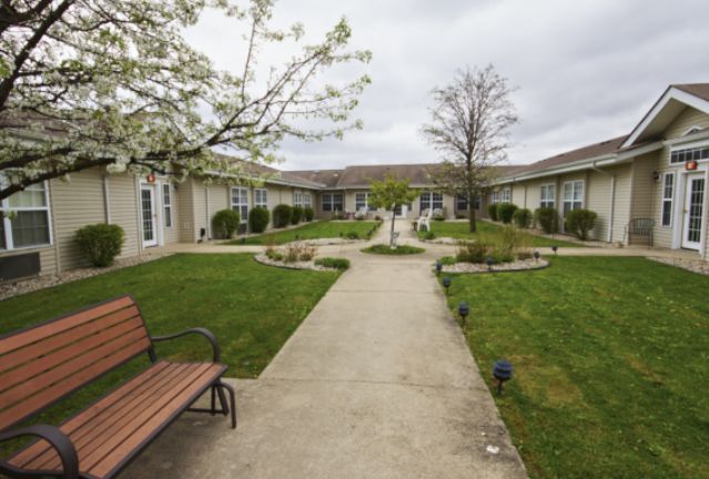 A serene courtyard with a central pathway, green lawns, and a bench surrounded by buildings.