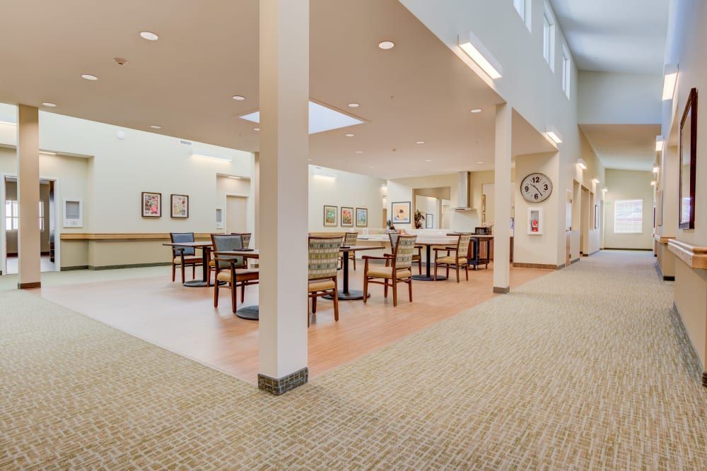 A spacious and well-lit dining area with tables and chairs, featuring pillars and a carpeted floor.