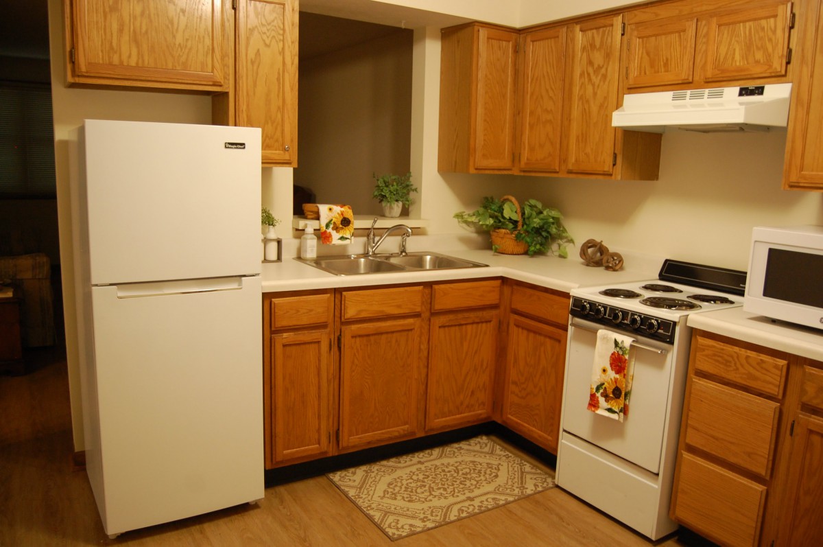 A cozy kitchen with wooden cabinets, a white refrigerator, stove, and various decorative plants on the countertop.