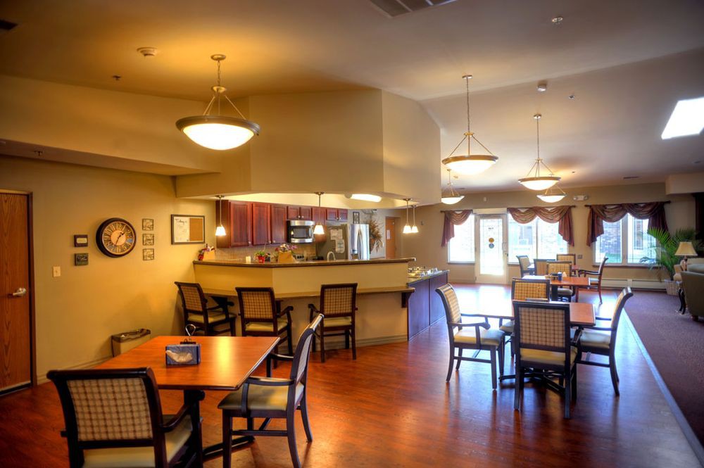 A cozy dining room with wooden tables and chairs, featuring a bar area and warm lighting.