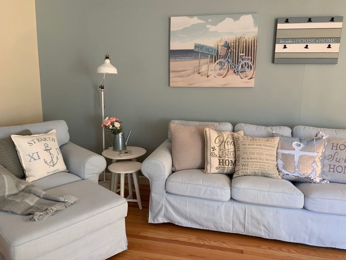 A cozy living room with a light blue sofa, decorative pillows, and coastal-themed paintings on the wall.