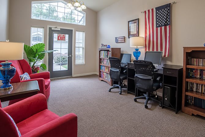 A cozy office space with computers, chairs, and an American flag, illuminated by natural light.