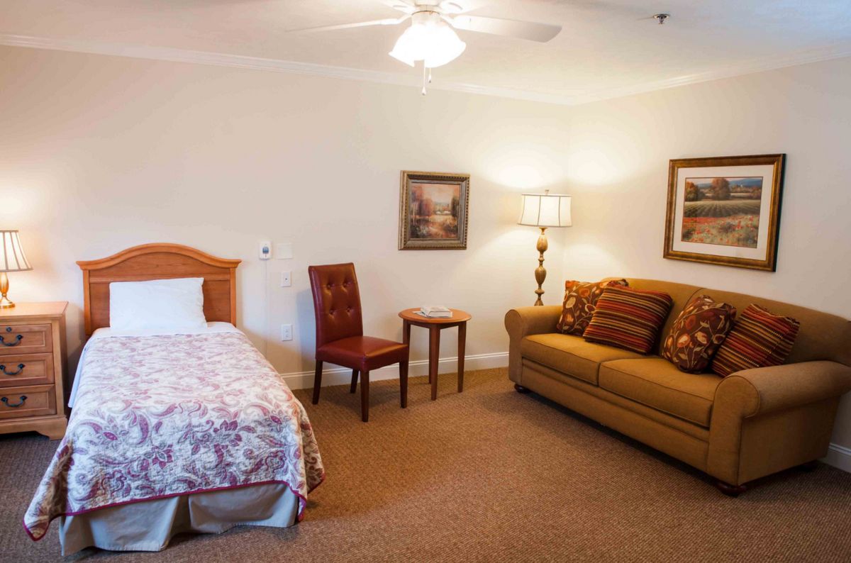 A cozy bedroom with a bed, sofa, chair, and decorative elements.