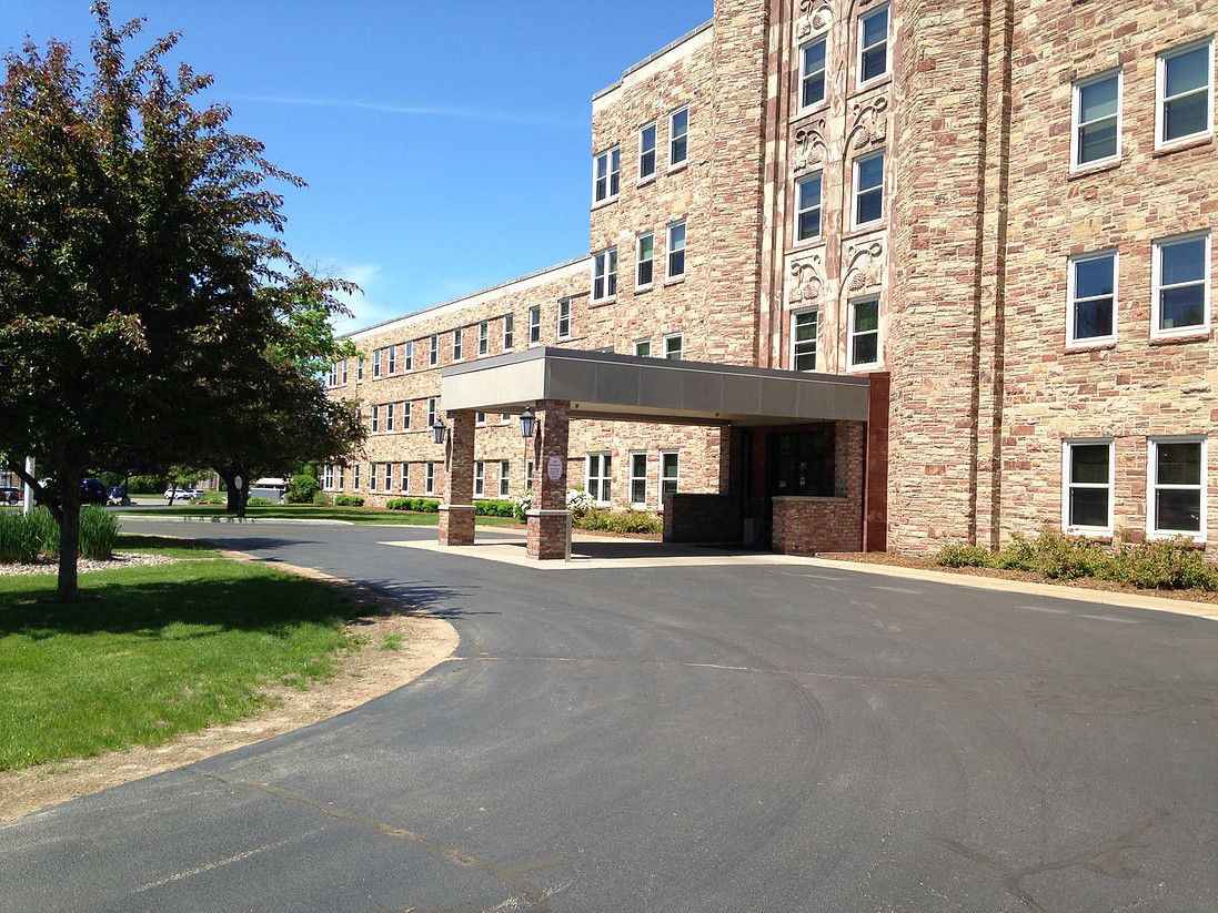 A stone building with a covered entrance and a surrounding driveway, set against a clear blue sky.