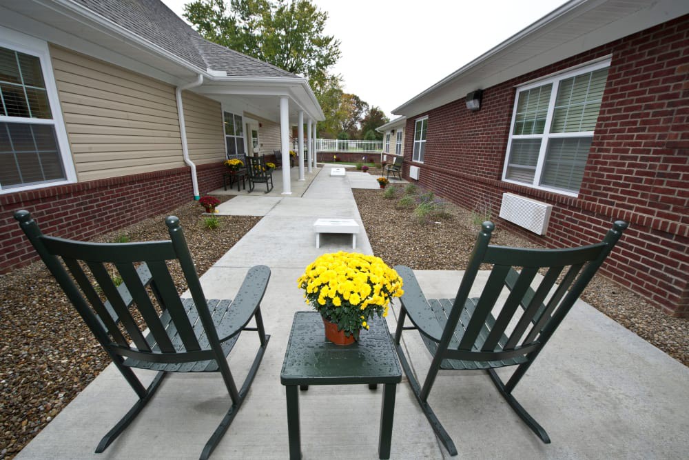 Two rocking chairs on a patio facing a walkway, with a table holding a pot of yellow flowers.