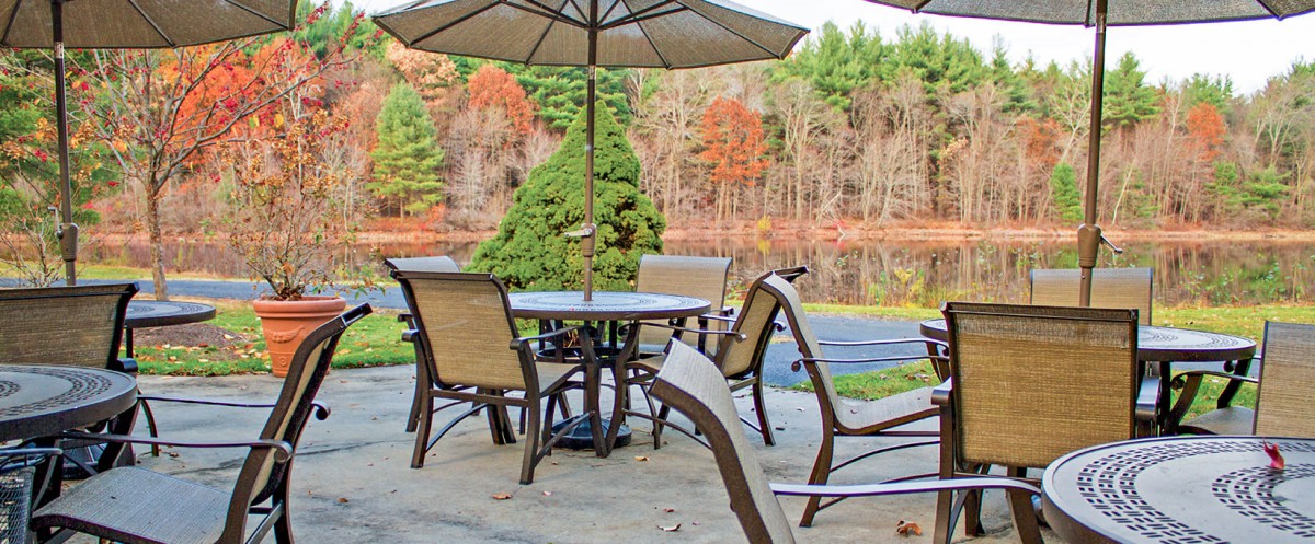 A patio setup with chairs and an umbrella overlooking a serene autumn landscape by a lake.