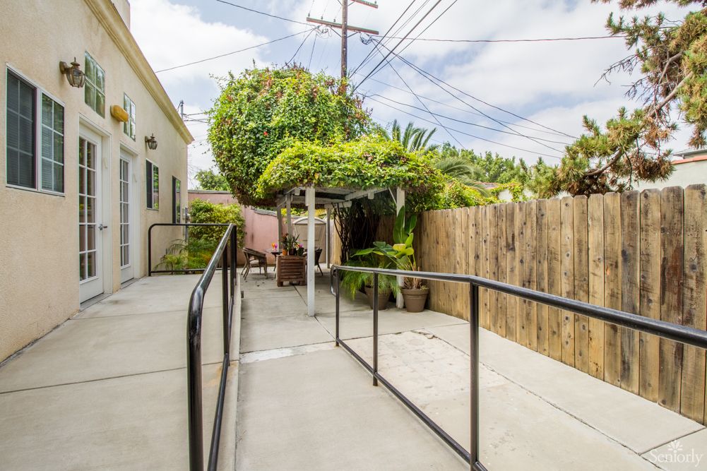 A backyard patio with a ramp, surrounded by a wooden fence and garden foliage.