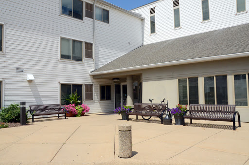 A sunny day at the entrance of a modern building, surrounded by colorful flowers and benches.