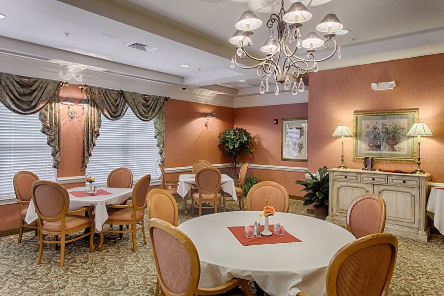 An elegant dining room with round tables, cushioned chairs, and a chandelier.