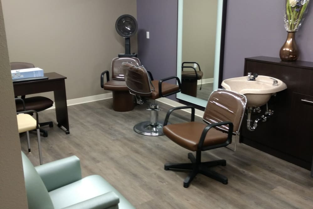 An empty hair salon with two chairs, a large mirror, and a sink.