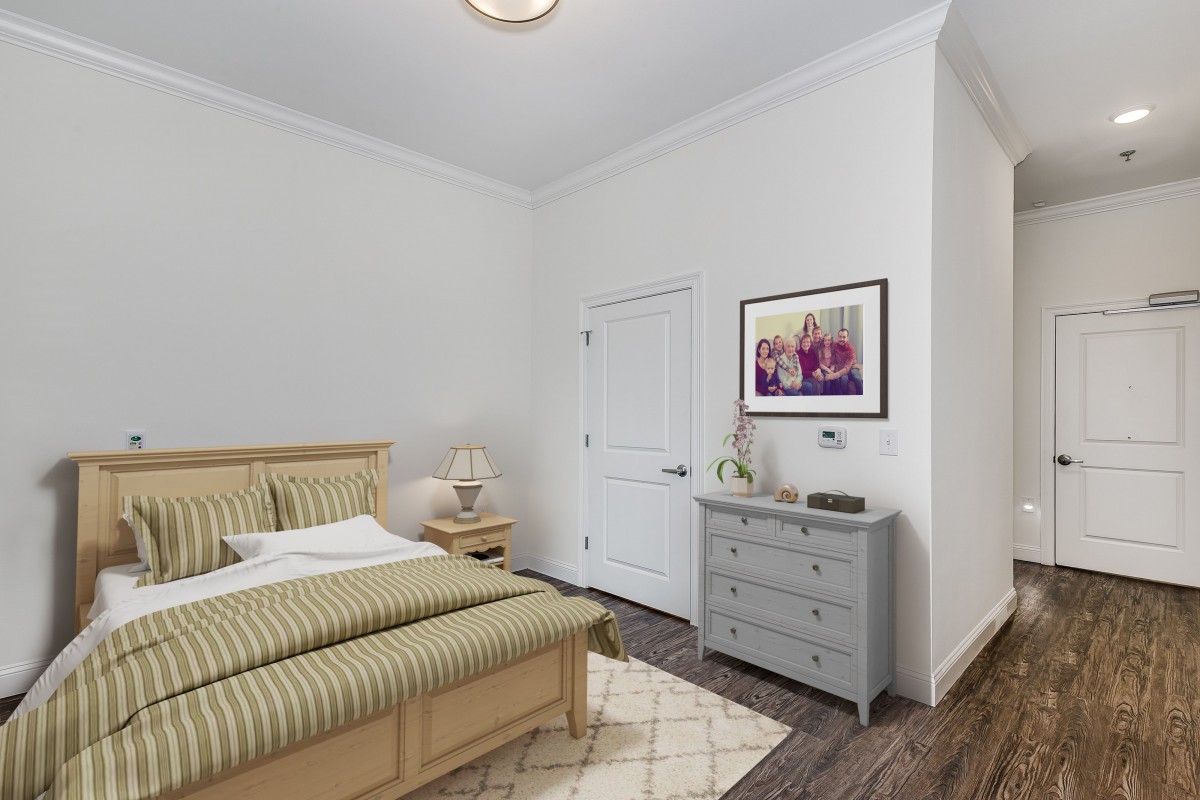 A cozy bedroom featuring a wooden bed with striped bedding, a bedside table with a lamp, and a gray dresser adorned with decorative items.