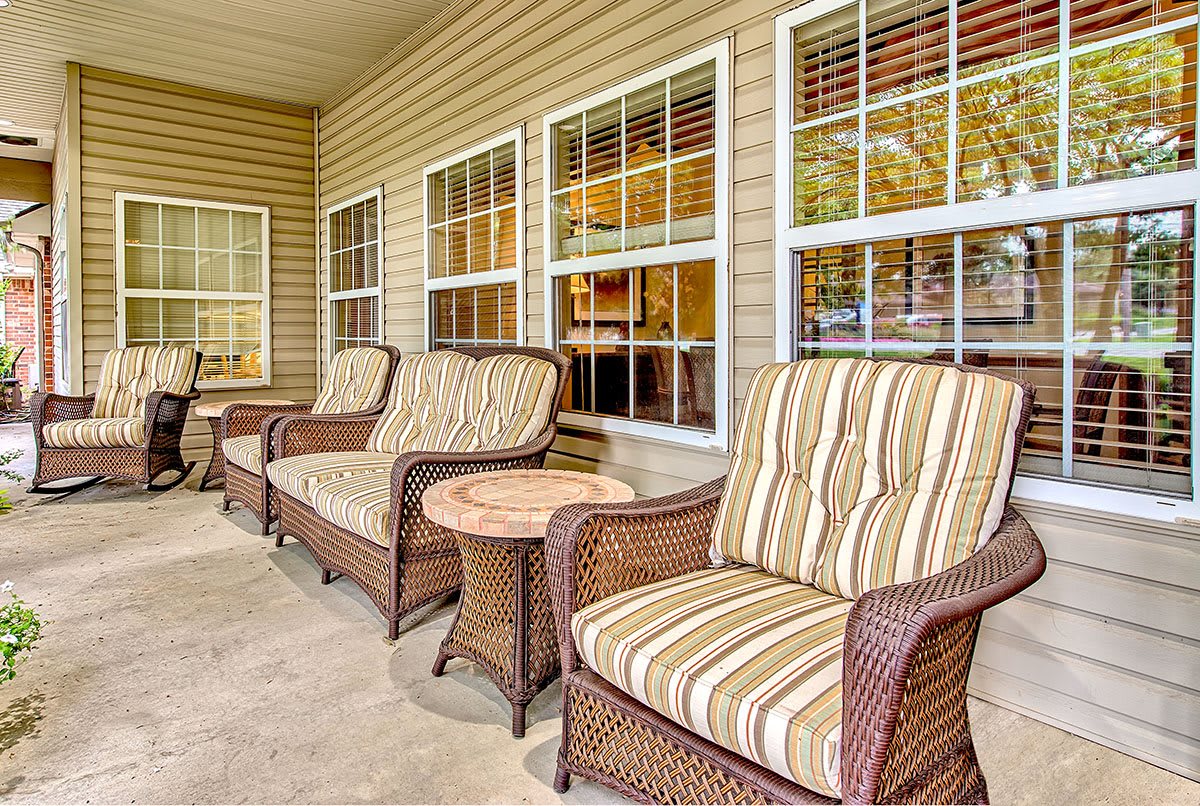 A cozy patio area with wicker chairs featuring striped cushions and a small side table, set against a backdrop of windows.