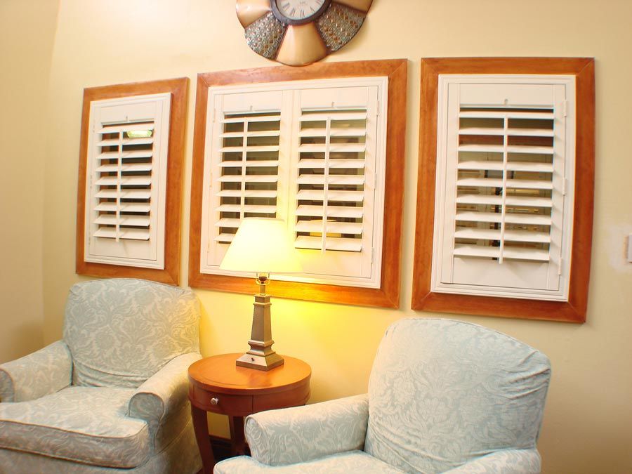 A cozy living room corner with two armchairs, a lamp on a side table, and decorative shutters on the wall.