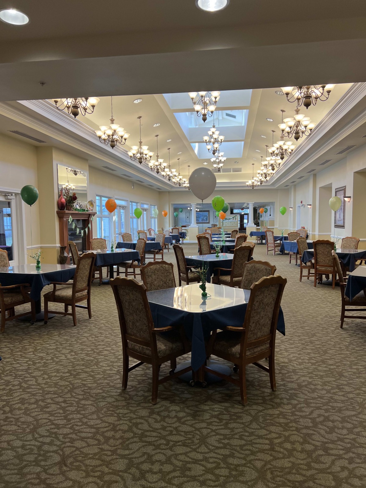 A spacious dining area with elegantly arranged tables and chairs, adorned with colorful balloons and illuminated by chandeliers.