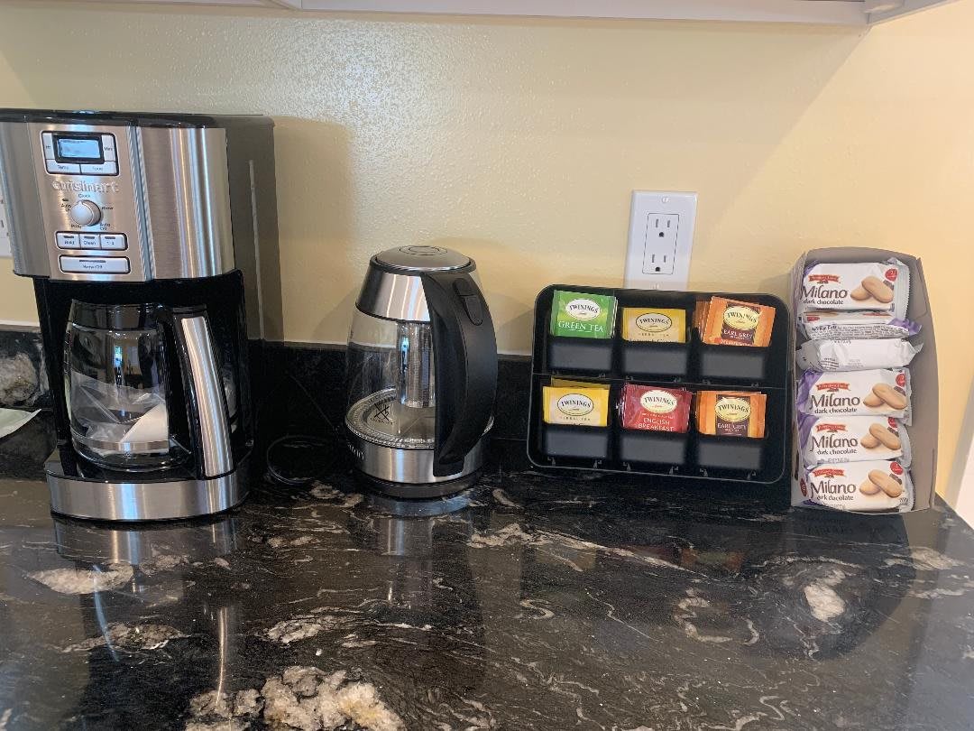 A kitchen counter with a coffee maker, electric kettle, assorted tea bags, and sugar packets.