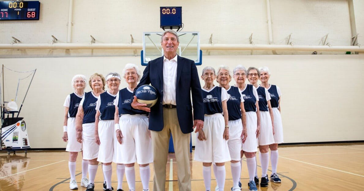 A senior women's basketball team posing with their coach in a gymnasium.