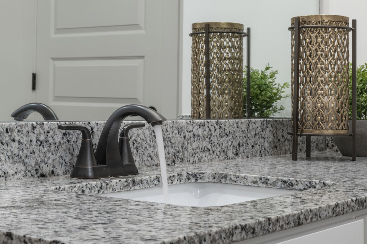 A bathroom sink with running water on a granite countertop, accompanied by decorative elements.