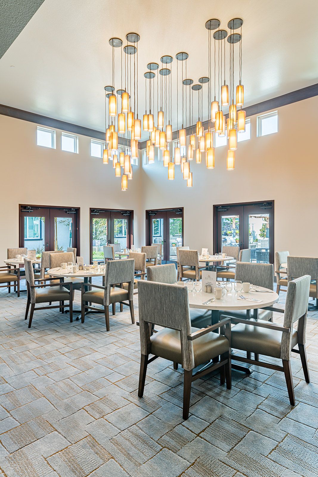 An elegantly designed dining room with a modern chandelier, featuring tables and chairs arranged neatly under warm lighting.