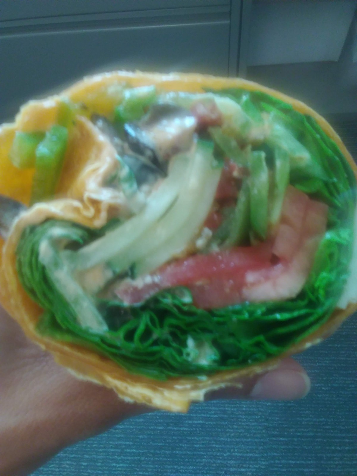 A close-up of a fresh vegetable wrap filled with greens, tomatoes, and other ingredients.