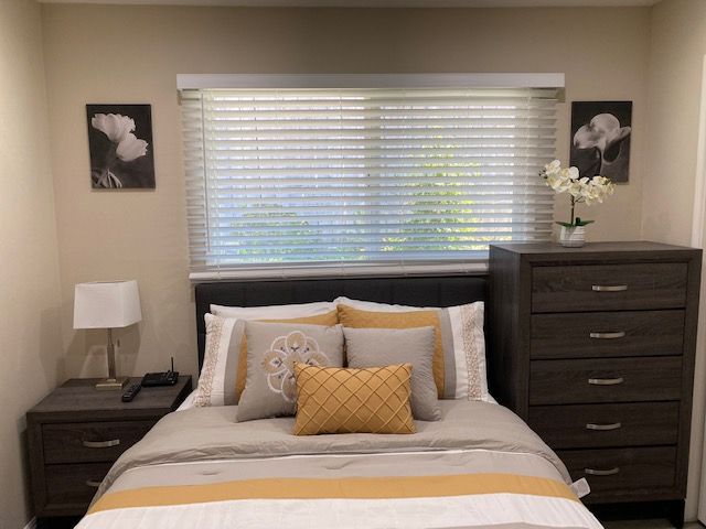 A cozy bedroom with a neatly made bed featuring yellow and gray accents, flanked by nightstands and a dresser.