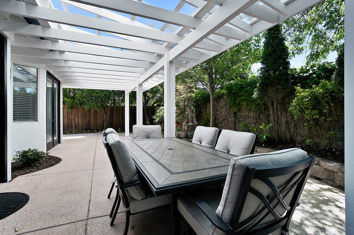 A spacious backyard patio with a pergola, featuring a large dining table and comfortable chairs.