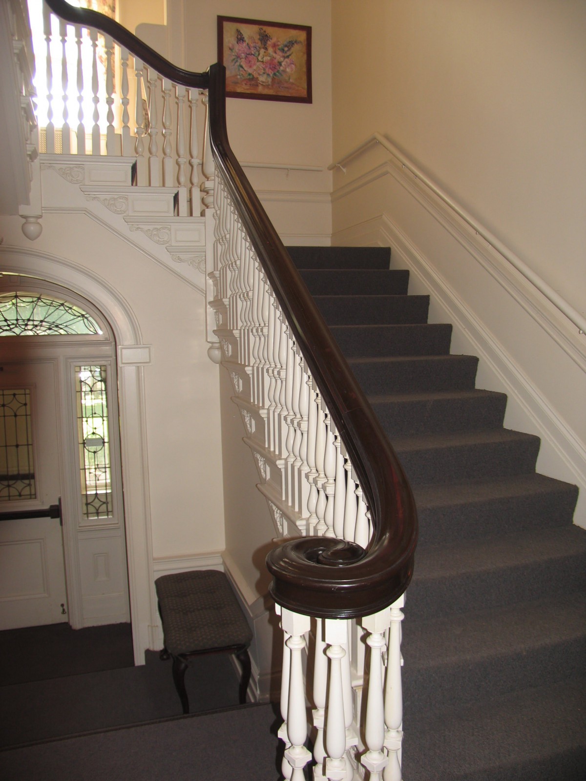 A classic interior staircase with a wooden banister and carpeted steps.