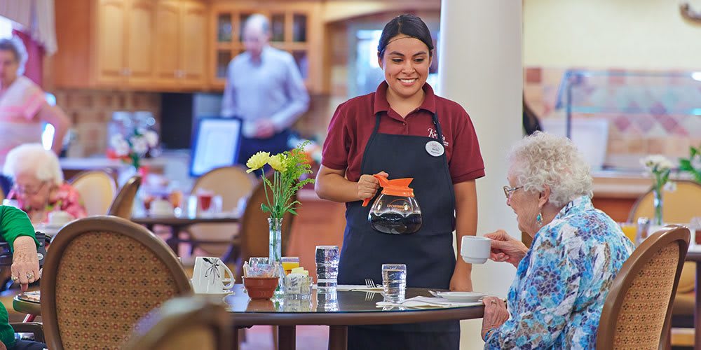 A waitress serves coffee to a customer at a restaurant, smiling warmly as she attends to the table.