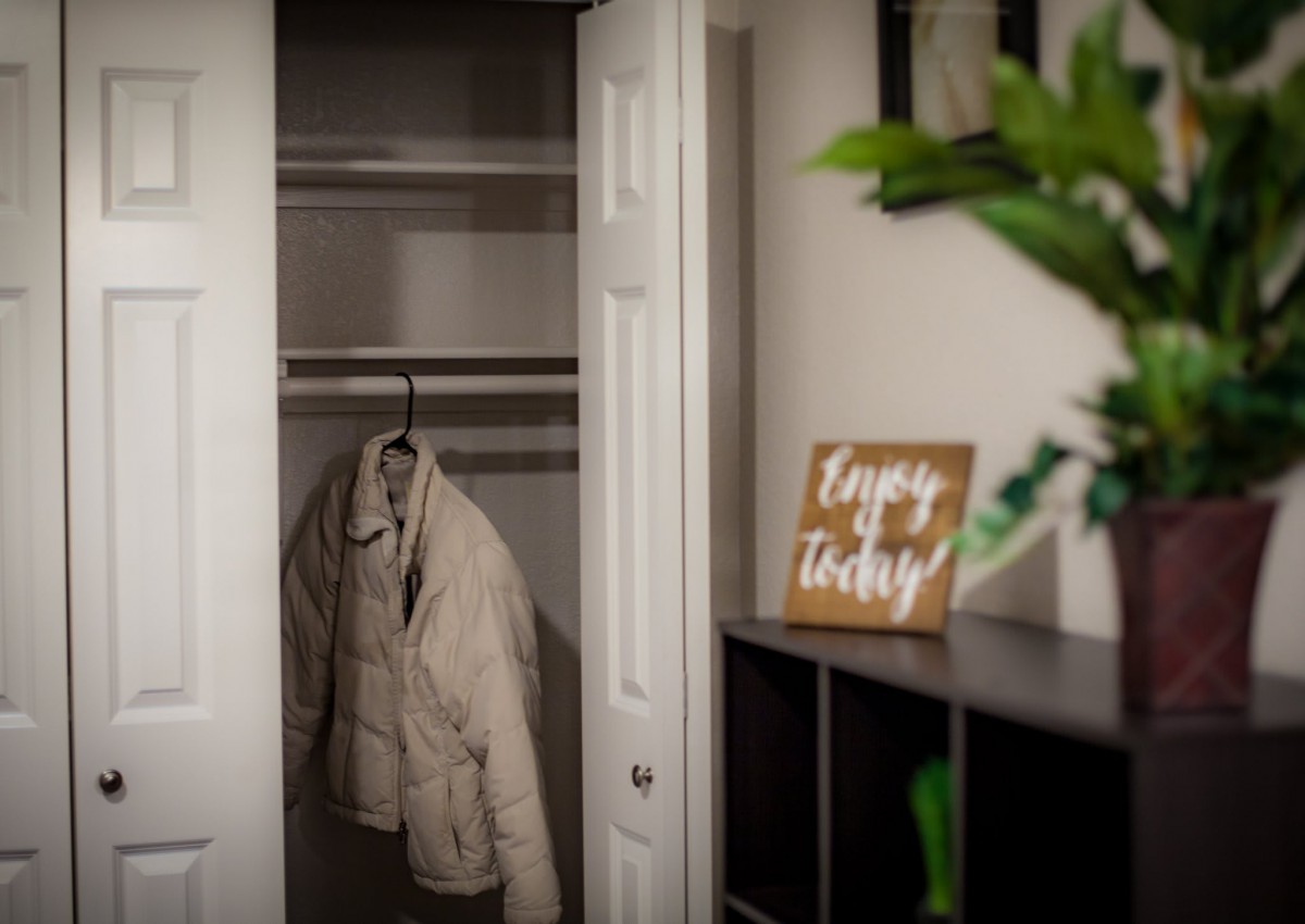 A cozy room corner featuring an open closet with a coat on a hanger, a motivational sign, and a potted plant.