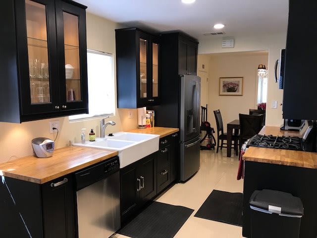 A modern kitchen with black cabinets and wooden countertops, leading into a dining area.