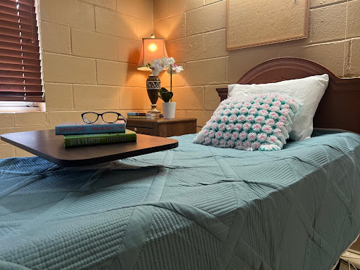 A cozy bedroom setting featuring a neatly made bed, a bedside lamp, and a stack of books.