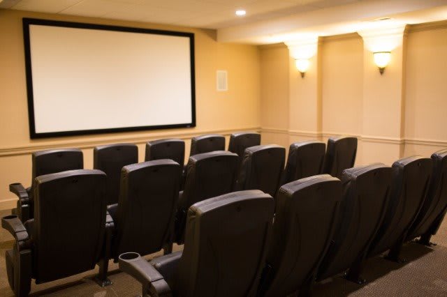 A cozy home theater setup with rows of comfortable chairs facing a large projector screen.
